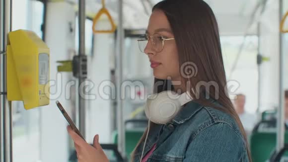 一个年轻微笑的女人在电车上用智能手机支付免费的公共交通视频的预览图