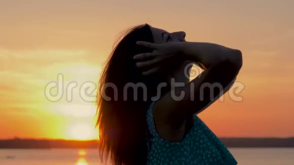在沙滩上一个穿着裙子坐在金色夕阳下的漂亮女人视频的预览图