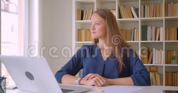 年轻迷人的白种人女商人的特写镜头她微笑着坐在办公桌前手提电脑视频的预览图