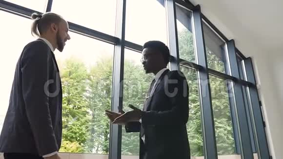 两位年轻的跨文化代表穿着西装讨论交易握手彼此问候视频的预览图