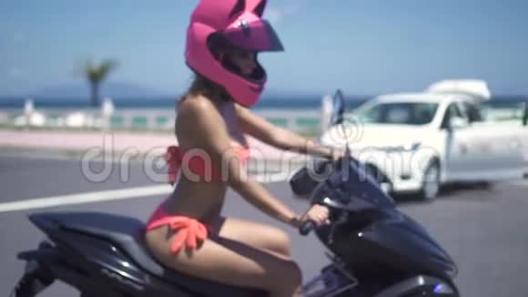 美丽的莫托女士穿着粉红色比基尼和头盔驾驶摩托车在海边景观慢动作美丽的女人视频的预览图