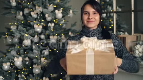 一幅美丽的深色头发的圣诞礼物的肖像她站在家里戴着装饰的新年树和视频的预览图