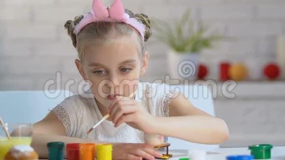 小女孩穿着可爱的头巾用明亮的颜料着色鸡蛋为孩子们提供艺术学校视频的预览图