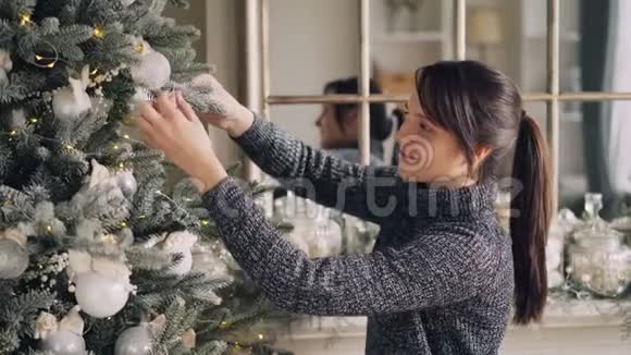创意棕发正在装饰圣诞树触摸美丽的球和照明聚会视频的预览图