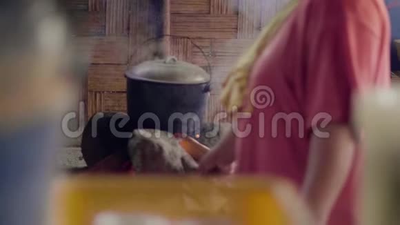 在亚细亚村一个女人用扇子吹火一边在篝火上做饭女人做传统晚餐视频的预览图