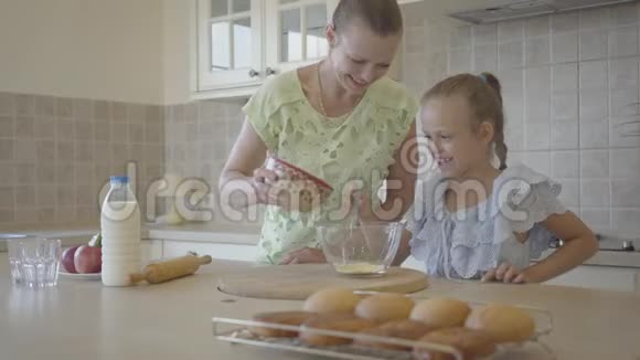 漂亮的年轻妈妈和可爱的小女儿一起在厨房做饭家庭幸福关系妈妈和女儿视频的预览图