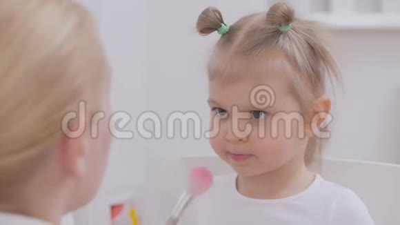 妈妈用刷子把粉末涂在她小女儿的脸上视频的预览图