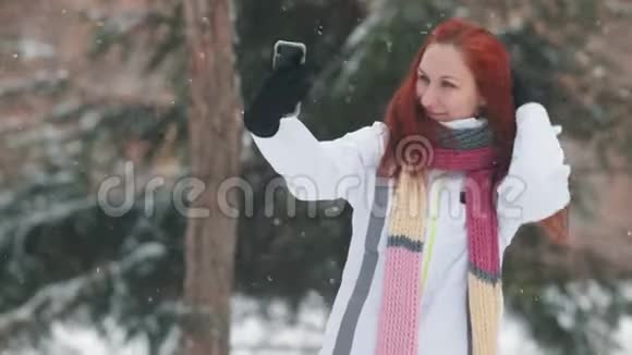 冬季公园一位留着鲜红头发的女人站在雪树面前自拍视频的预览图
