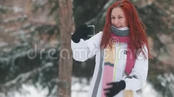 冬季公园一个红发鲜艳的女人站在雪树面前自拍大雪视频的预览图