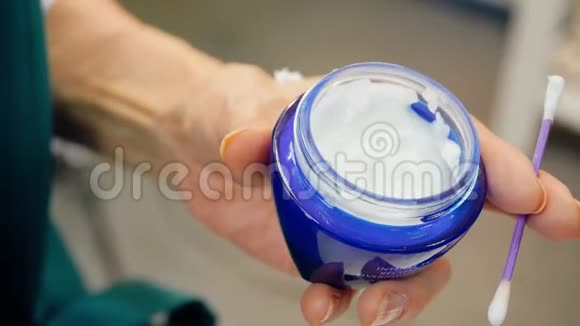 老妇人手里拿着一个蓝色的奶油罐和一根棉花棒视频的预览图