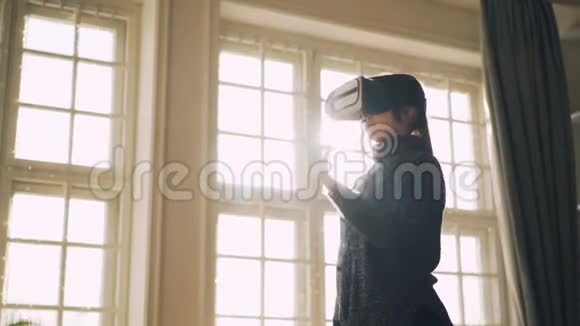 穿着毛衣的年轻女孩笑着玩虚拟现实眼镜双手站在灯光工作室里视频的预览图