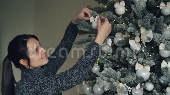 微笑着漂亮的女孩正在圣诞节前装饰新年树触摸银球和灯光享受着快乐视频的预览图