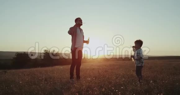 泡泡时间爸爸和他的小男孩在大自然中制作泡泡令人惊叹的日落视频的预览图