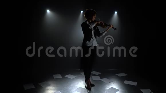 黑暗工作室的女孩拉小提琴在地板上的纸条剪影黑烟背景视频的预览图