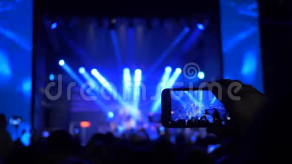 手持智能手机的歌迷们在夜间泛光灯下的摇滚音乐会上拍摄照片和录像视频的预览图