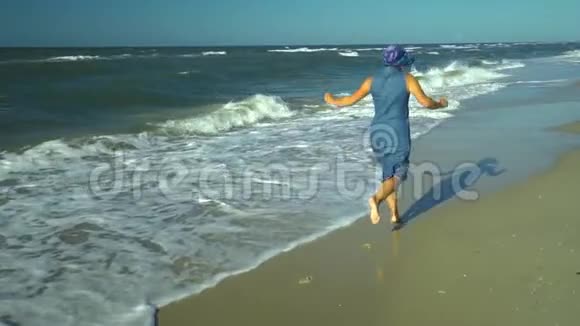 年轻漂亮的女人沿着海滨跑她高兴沙滩和海浪慢动作女人微笑这就是视频的预览图