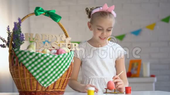 穿着白色连衣裙的创意女孩展示彩绘复活节彩蛋装饰篮桌视频的预览图