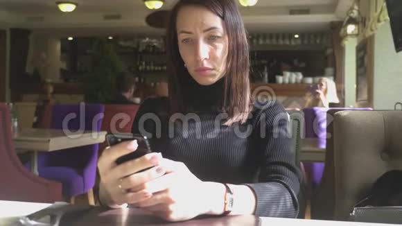 年轻的馄饨在工作休息的时候坐在舒适的咖啡店里一边用手机一边迷人的快乐女性阅读视频的预览图
