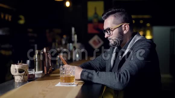 在酒吧柜台上的一杯饮料旁使用智能手机的人视频的预览图