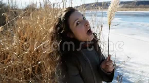 一个美丽的女孩在冰冻的河岸上欣赏大自然的肖像笑着玩着黄藤视频的预览图