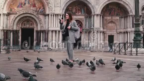 快乐兴奋的女游客与鸽子坐在手臂上拍摄智能手机照片在城市广场威尼斯慢动作视频的预览图