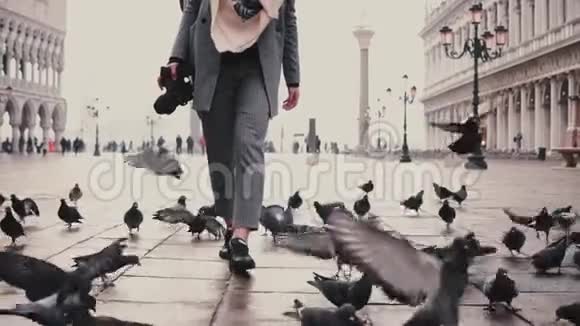 在圣马可广场上带着一群鸽子在威尼斯慢动作漫步带着相机散步的美丽女游客快乐视频的预览图