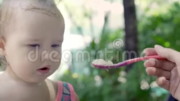 一岁的女孩在棕榈树附近吃一勺粥热带慢动作视频的预览图