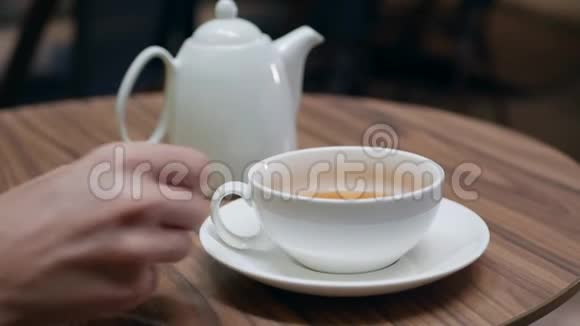 那个穿黄色衣服的女人正在夏天的咖啡馆里喝茶白色杯子和茶壶特写镜头4k视频的预览图