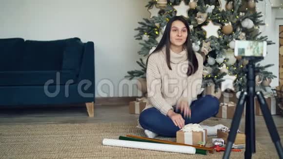 一位富有创造力的年轻女士正在为在线视频博客录制有关圣诞节礼物包装的视频女孩在展示视频的预览图