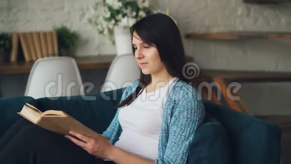平静的女孩正坐在家里的沙发上看书翻开书页享受和平文学和舒适不错的阁楼风格视频的预览图