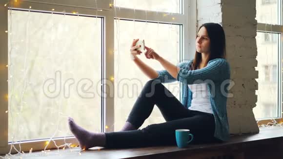 女孩在网上和朋友聊天用智能手机打视频电话坐在窗台上谈笑风生视频的预览图