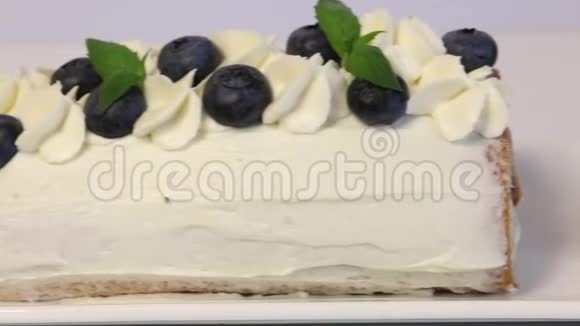 海绵蛋糕涂上奶油用干蓝莓和新鲜薄荷叶装饰特写镜头视频的预览图