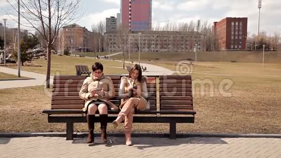 母女俩坐在公园的长凳上用手机视频的预览图