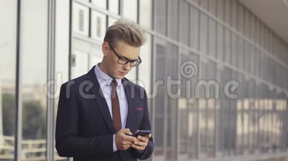 快乐的商人微笑着看着站在办公室外面的短信时尚的男性执行经理视频的预览图