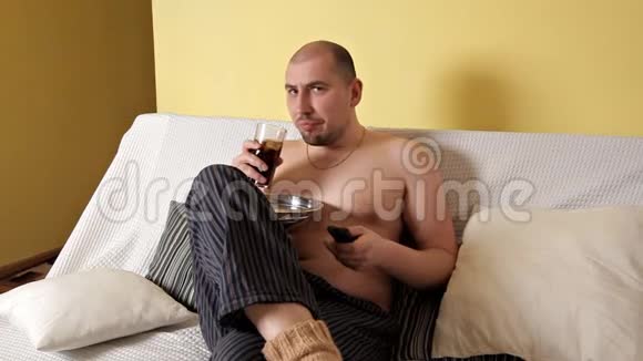一个又胖又秃又懒的男人吃薯片喝可乐坐在沙发上没有外套一个卑鄙的人有害视频的预览图