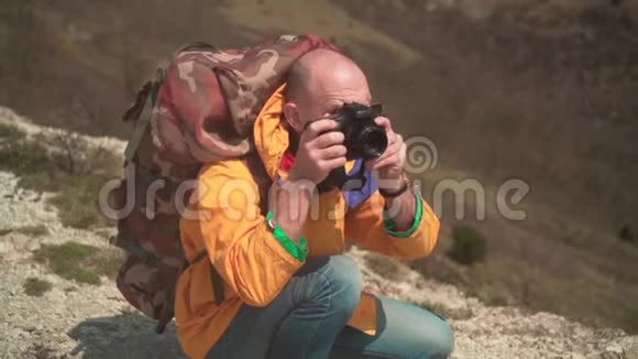 一个穿着黄色夹克和眼镜的人站在山上欣赏风景在dslr相机上拍照视频的预览图