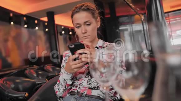 年轻的法国女性使用社交网络与手机通信坐在皮椅上的餐厅里视频的预览图