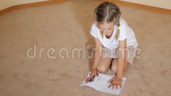 小女孩坐在地上拿着纸在家里拿着水彩画画视频的预览图