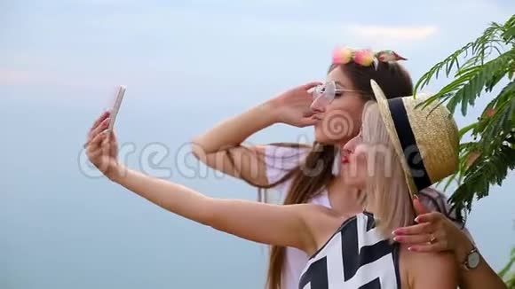 积极的女孩金发碧眼的金发碧眼的黑发女郎用手机在岩石悬崖的绿树旁拍照视频的预览图