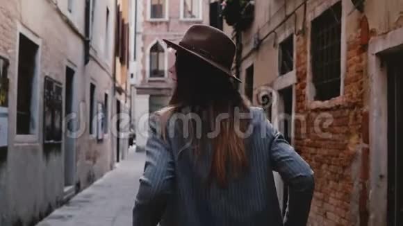 在意大利威尼斯自信时尚的年轻女商人戴着帽子和西装走在狭窄的古老街道上视频的预览图