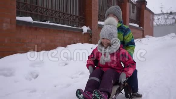 冬天的娱乐活动小男孩和小女孩骑着雪橇沿着下雪的路视频的预览图