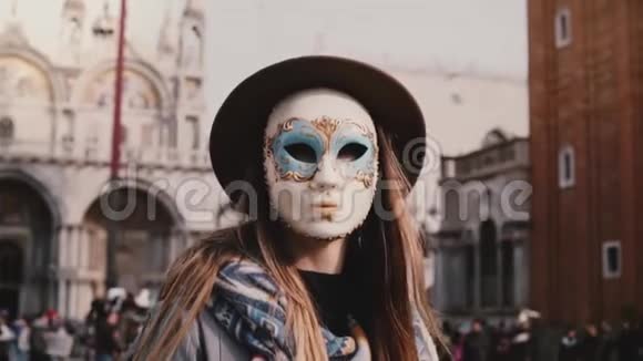 一位留着长发的女游客戴着传统的嘉年华面具站在威尼斯圣马可市广场慢动作视频的预览图