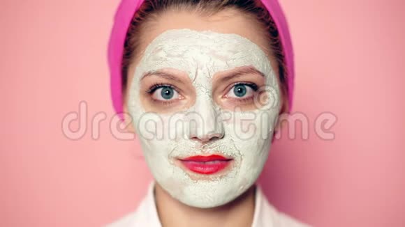 靠近一个脸上戴着面具的女孩她在粉红色的背景下吃苹果护肤及清洁的概念视频的预览图