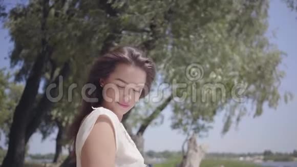 一位美丽的少女一头深色长发穿着一件白色的夏装站在河边视频的预览图