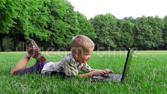 6岁的孩子拿着笔记本电脑躺在草地上视频的预览图
