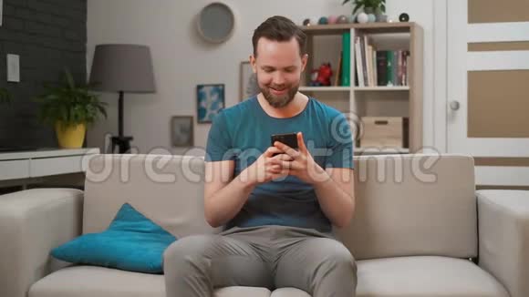 年轻英俊的白种人使用现代手机坐在家里的沙发上两人都拿着手机视频的预览图