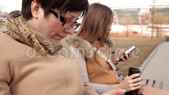 母女俩坐在公园的长凳上用手机视频的预览图