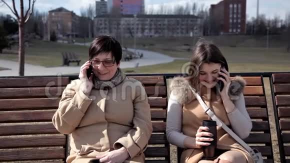 母女俩坐在公园里的长凳上用手机说话家人时间散步视频的预览图