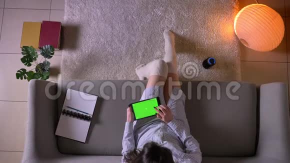 年轻迷人的女性在平板电脑上发短信的特写镜头绿色的彩色屏幕坐在可爱的沙发上视频的预览图