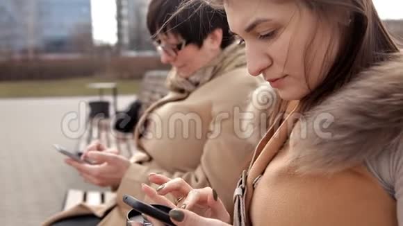 母女俩坐在公园里用手机写短信视频的预览图